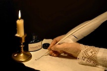 female hand using a feather scribe to write on paper by candelight