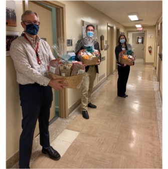 three people wearing masks holding gift baskets