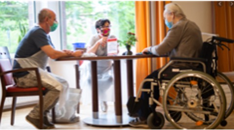 three senior citizens sitting around a table wearing masks