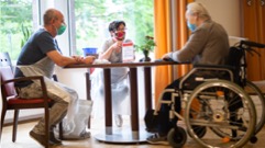 three senior citizens sitting at a table wearing masks