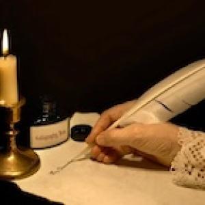 female hand using a feather scribe to write on paper by candelight